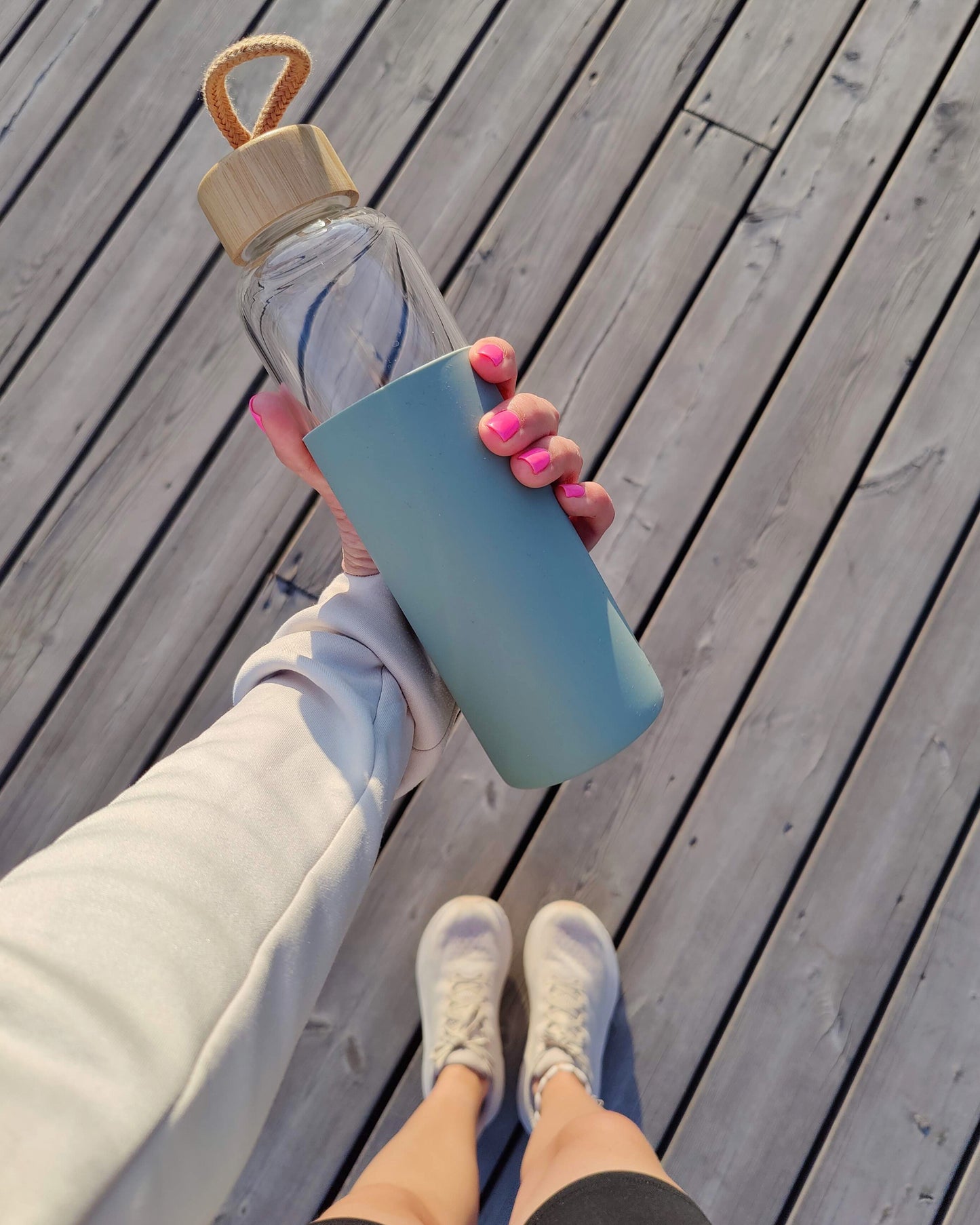 Borosilikaattilasi pullo bambukorkilla ja pastellin vihreällä silikonisuojalla. Naisen kädessä