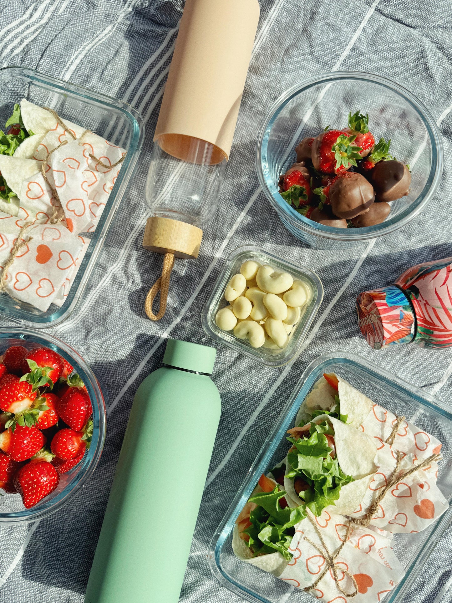 Pastellinvihreä teräsjuomapullo ja lasipullo Pastellin vaaleanpunaisella silikoni suojalla vaaka-asennossa osana piknik kattausta