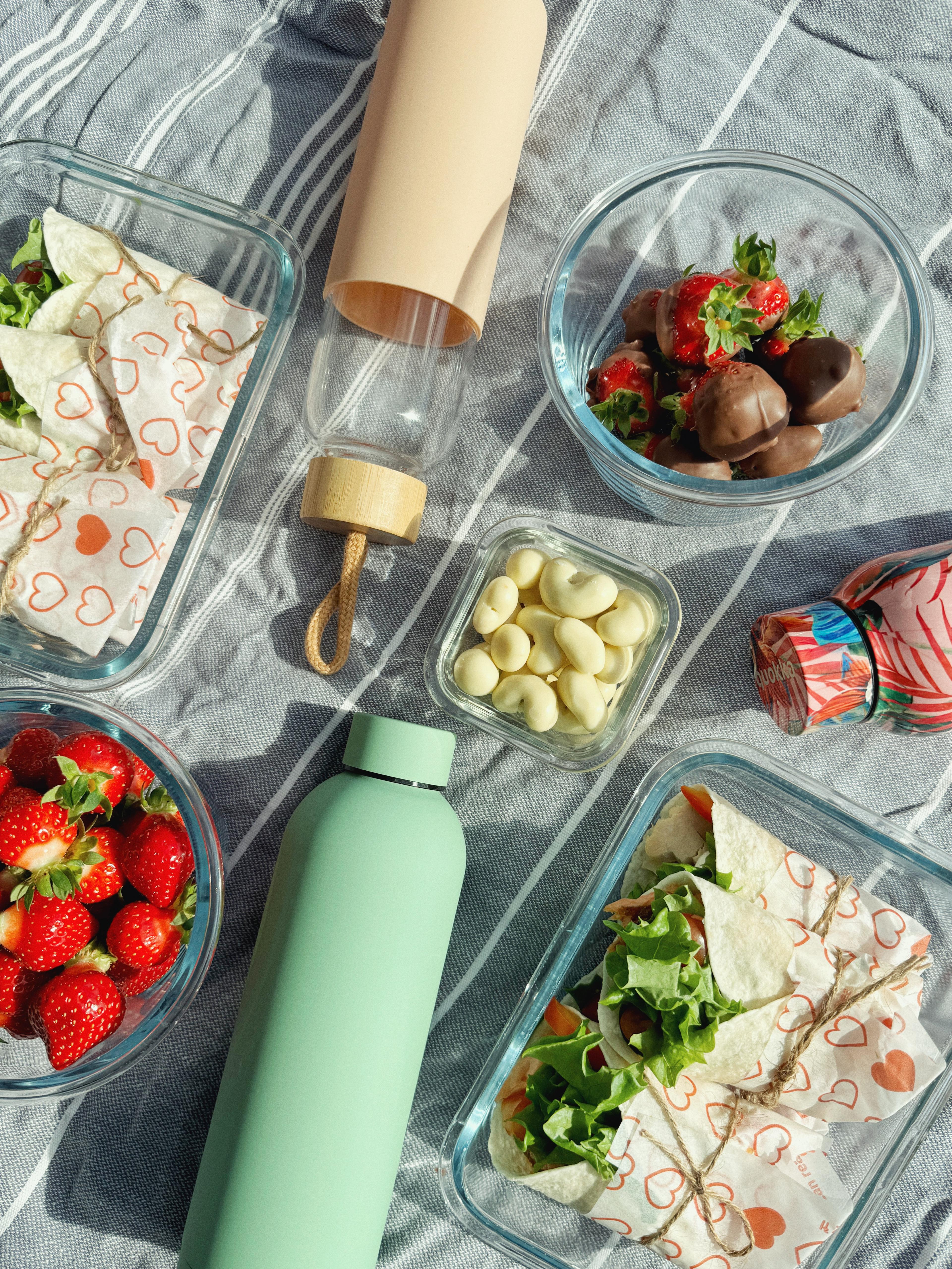 Pastellinvihreä teräsjuomapullo ja lasipullo Pastellin vaaleanpunaisella silikoni suojalla vaaka-asennossa osana piknik kattausta