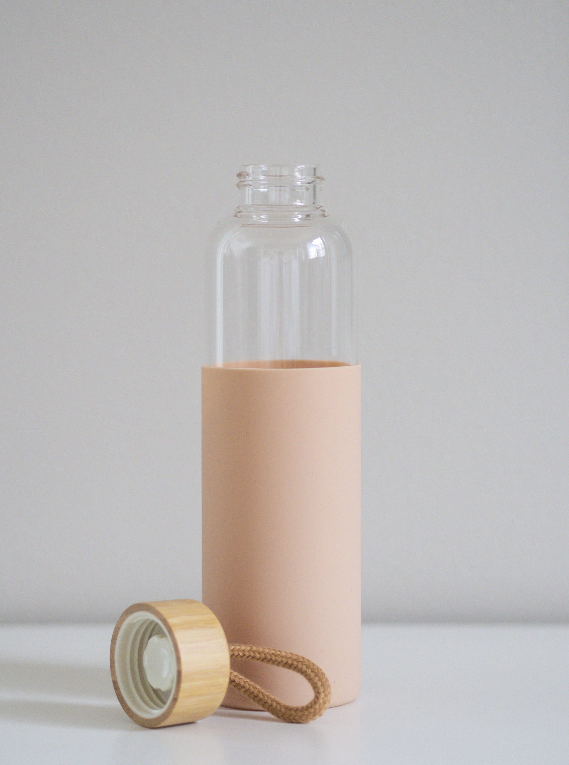 Pastellin vaaleanpunainen lasipullo silikonisuojalla ja bambukorkilla