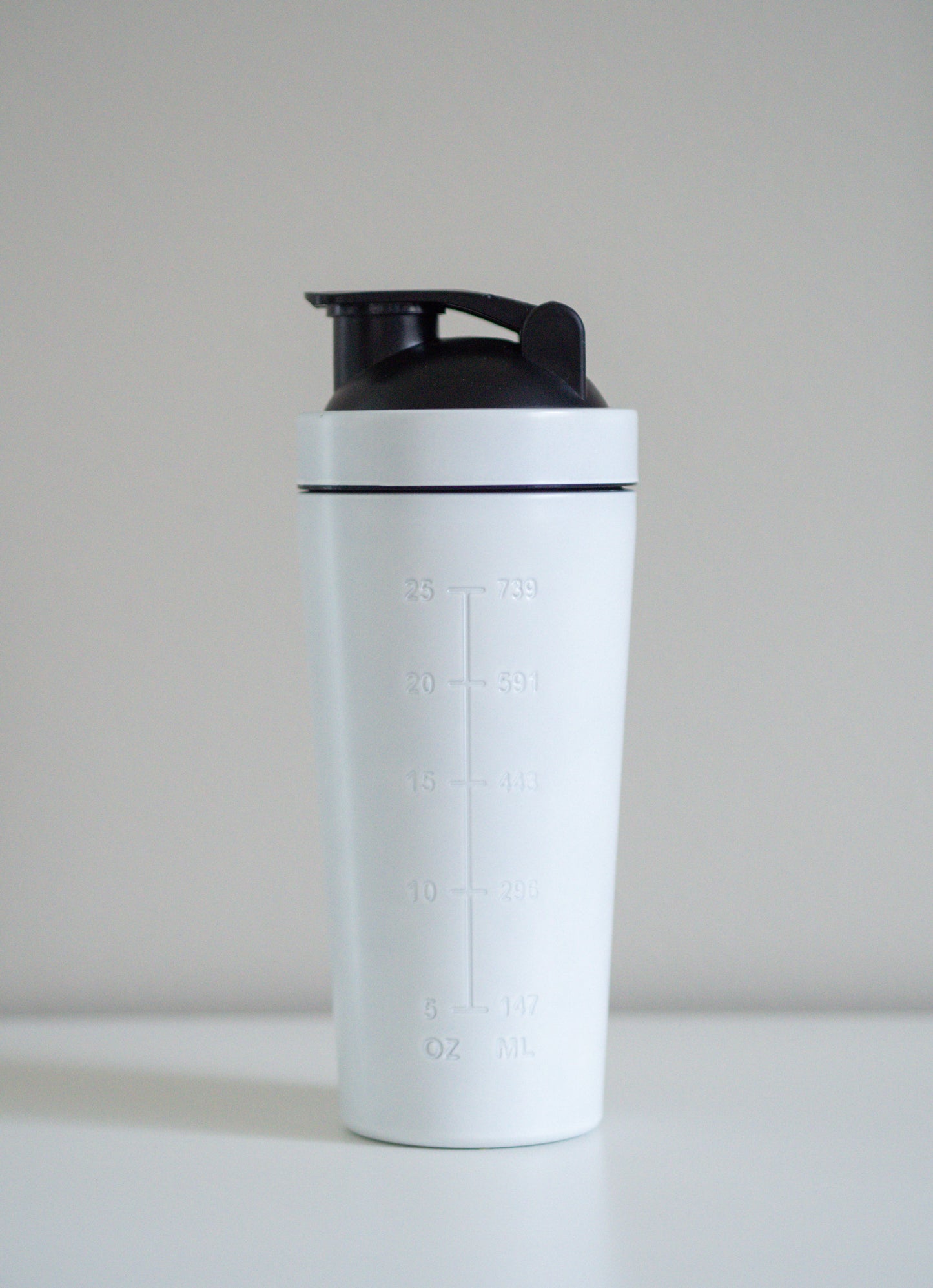 Minimalistinen ja moderni valkoinen terässheikkeri, joka erottuu edukseen perinteisistä muovimalleista – mukana metallikansi ja sekoituspallo.