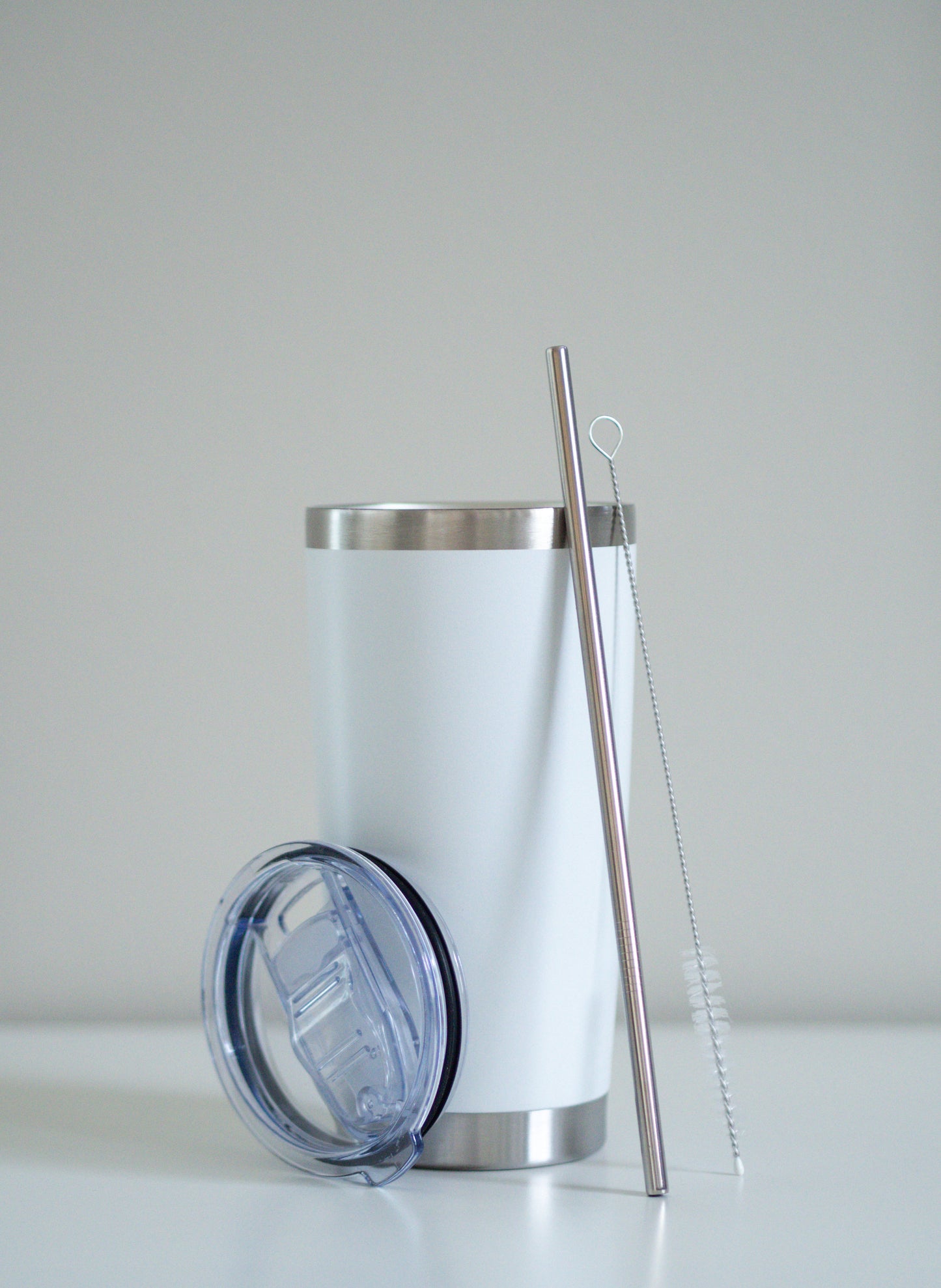 Classic White -terästumbleri, johon nojaa ruostumaton teräspilli, puhdistusharja ja läpinäkyvä muovikansi